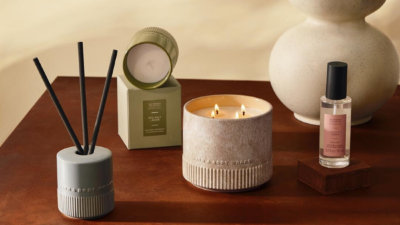 Bath & Body Works Reserve Collection products styled on a wooden table, including a lit three-wick candle, a reed diffuser, a boxed Sea Salt + Musk candle and a Vanilla + Tonka room mist.